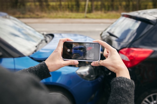 female driver taking photos of road traffic accident on mobile phone for insurance claim