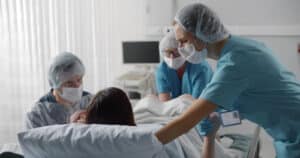 Back view of medical staff in protective uniform helping pregnant woman in labor